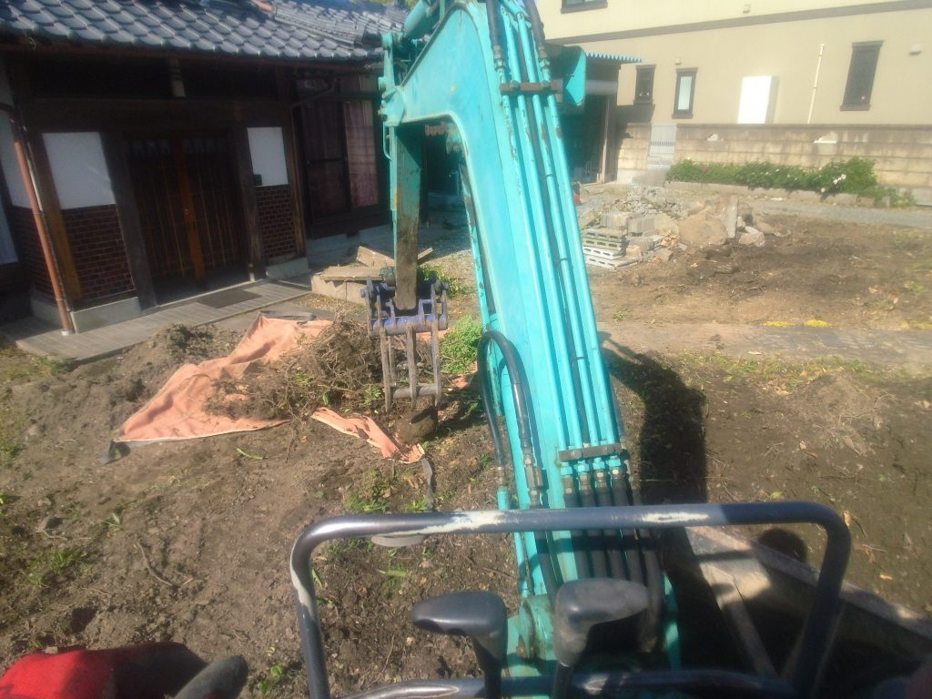 フォークバケットで摘んだ枝や根を、土を振るってもっこに入れてます